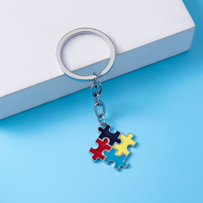Metal keychain with colorful puzzle piece charm on blue background, sensory accessory